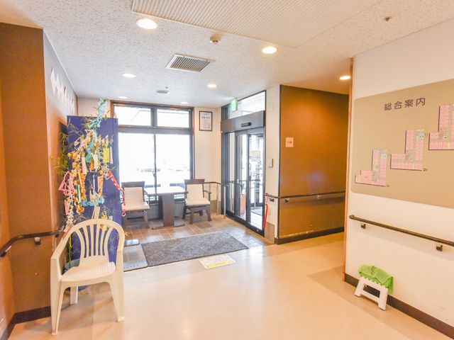 エントランスホールの様子 出入り口 ゆったりとした座席が配置された明るいエントランスホールです。人々の往来や笑顔が見られ、温かい雰囲気が漂っています。