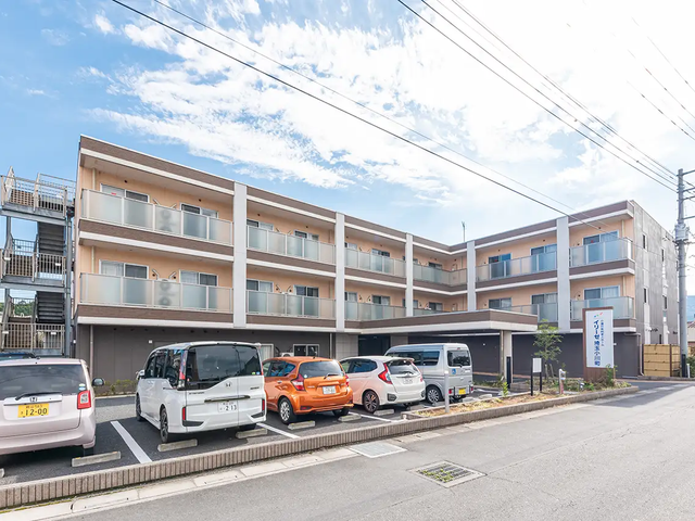 清潔感のある施設外観 外観 広くて開放的な入り口が特徴的な建物で、訪れる方々を明るく迎え入れています。白と茶色を基調とした色合いが落ち着いた雰囲気を醸し出しており、就業にあたりイメージがしやすい環境です。