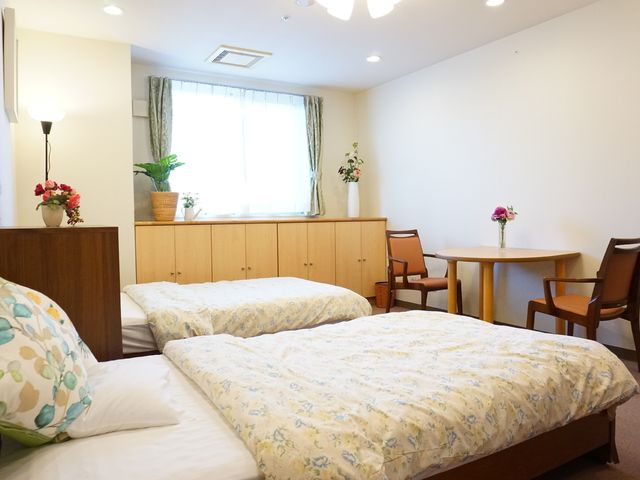 快適な居室の一例 居室 窓辺の明かりが柔らかな居室です。清潔感のあふれるベッドとテーブルが配置され、落ち着いた時間を過ごせそうです。