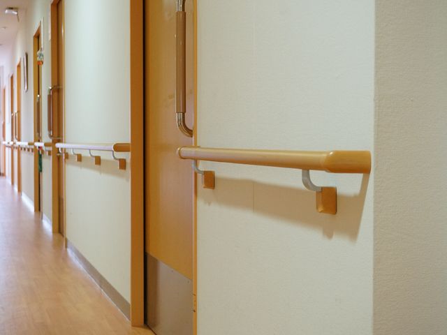 廊下の手すりとドア 廊下 手すりが設置された安全で清潔な廊下です。利用者の方々の移動をサポートしながら、日々の業務に携われる環境が整っています。