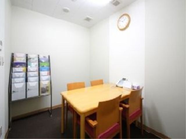 シンプルな掲示物部屋 相談室 壁に掲示物が整然と掛かり、清潔感のある会議スペースが広がっており、穏やかな時間が流れている様子が伺えます。