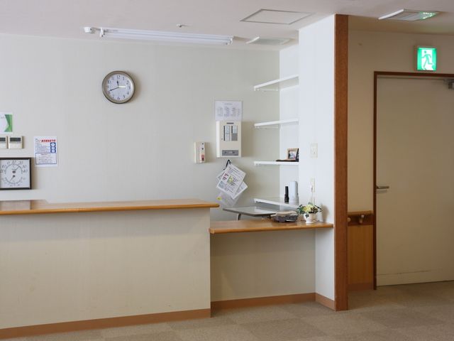清潔なカウンターと時計 受付 木のぬくもりを感じる明るい受付カウンターがあります。利用者の皆様の安心を支える一角として、丁寧な対応を心がけています。