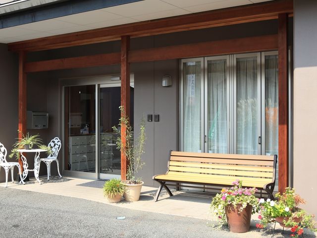快適なエントランス風景 入口 ベンチと植物が配置された落ち着いた雰囲気のエントランスです。温もりと安らぎが感じられる空間になっています。