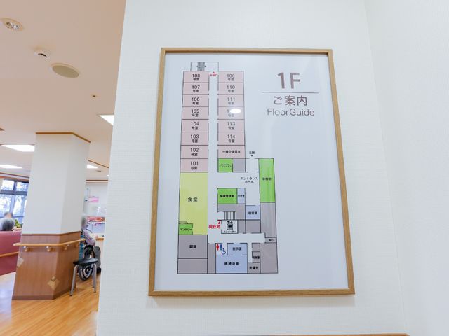 施設フロアガイド案内図 案内図 整備されたロビーには案内図が掲示され、車椅子を利用される方が背景に見えます。安心して業務に取り組める環境が整っています。