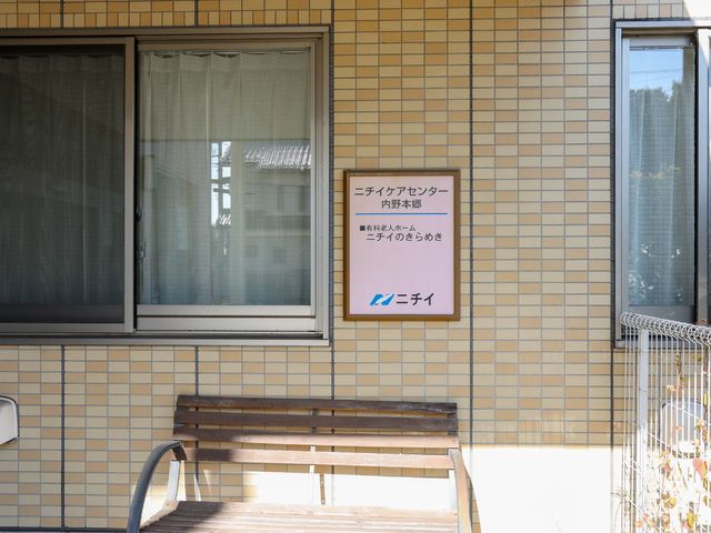 看板付きの明るいエントランス エントランス 手すり付きのベンチが配されたエントランスは、来訪者を温かく迎えます。明確な表示がある入口は、利用者とスタッフの快適な出入りを支えています。