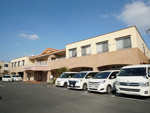 広々とした駐車場付き建物 外観 明るい天気の下、清潔感あふれる建物が迎えてくれます。広々とした駐車スペースも完備されており、アクセスも良好です。