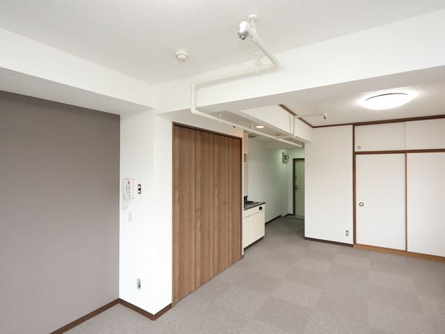 洋室のキッチンと入口 居室 広々とした居室には、キッチンが備え付けられ、自由に生活空間を使いこなせます。スタイリッシュな扉のデザインが、落ち着いた雰囲気を演出しています。