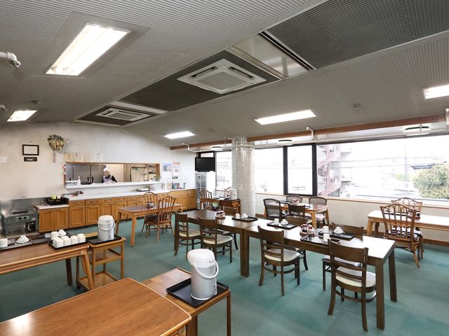 食事スペースの清潔なダイニング 食堂 清潔感のあふれる食堂で、入居者がお食事を取られています。調理スペースが見え、開放的な雰囲気が広がっています。