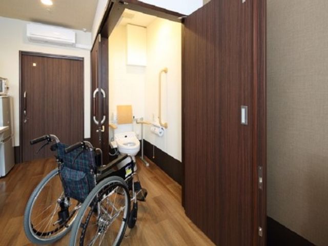 バリアフリートイレと車椅子 居室・トイレ 手すり付きの広々としたトイレスペースは、利用者が安心して日常生活を送れるよう配慮されています。車椅子もすんなりと入ることができます。