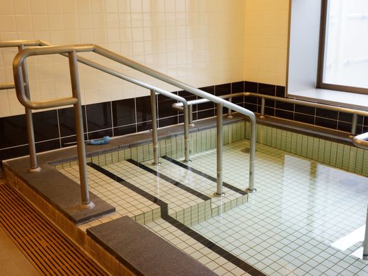 大浴場には、手すりやステップが備わったタイル張りの大型浴槽が設置されている。自然光が差し込む大きな窓がある。