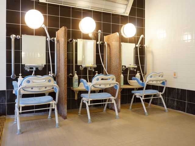 清潔な洗面台設備 大浴場 広々とした洗面スペースは快適な身支度をお手伝いします。明るい照明と手すり付きの座席で、安全にご利用いただけます。