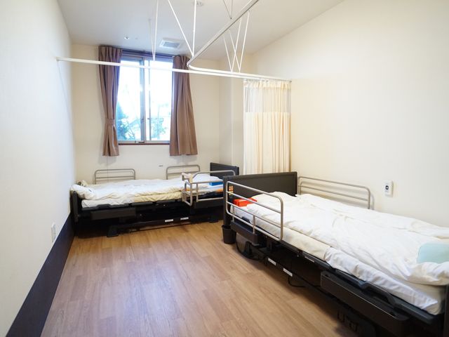 明るい病室のベッド 居室 心地良い光が差し込む居室です。調節可能なベッドで快適な療養生活を支えます。