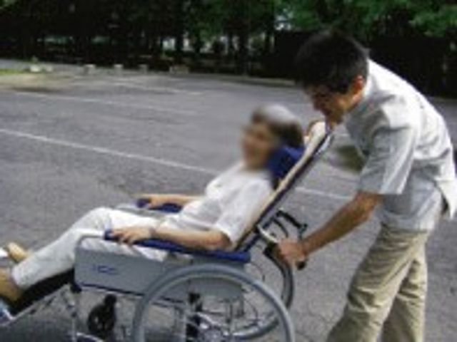 車椅子を押す様子の外観 外観 屋外で、スタッフが丁寧に車椅子を押す光景です。安心してサポートを受けられる環境が整っています。