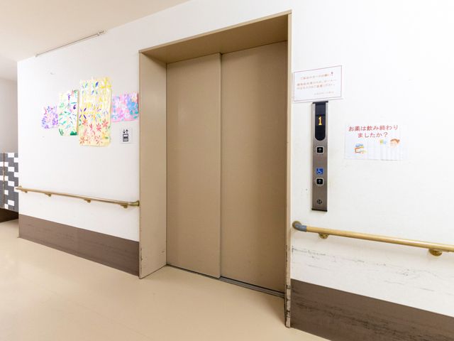 エレベーター前の廊下 廊下   手すりが両側に設置された、移動しやすい廊下です。壁面の掲示や飾りがあり、明るい雰囲気が伝わります。