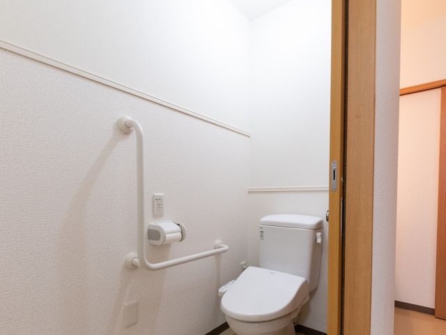手すり付きトイレ トイレ   手すりが設置された明るいトイレです。出入口も広めで、利用しやすさに配慮されています。