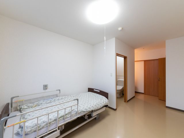 明るい個室の居室 居室   シンプルで明るい個室です。ベッドのそばにトイレがあり、日常の動線に配慮されたつくりに見えます。