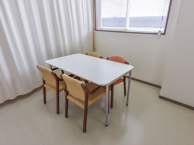 シンプルな居室のテーブルと椅子 談話室 シンプルで清潔感のある居室です。窓からの自然光が明るい雰囲気を演出しており、静かに過ごせる環境が整っています。