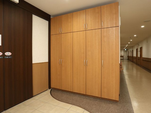 廊下の木目調扉 玄関 ゆとりある廊下が、心地よい職場環境を創り出しています。端に座る方が、休息を取りながら穏やかな時間を過ごされている様子が伺えます。