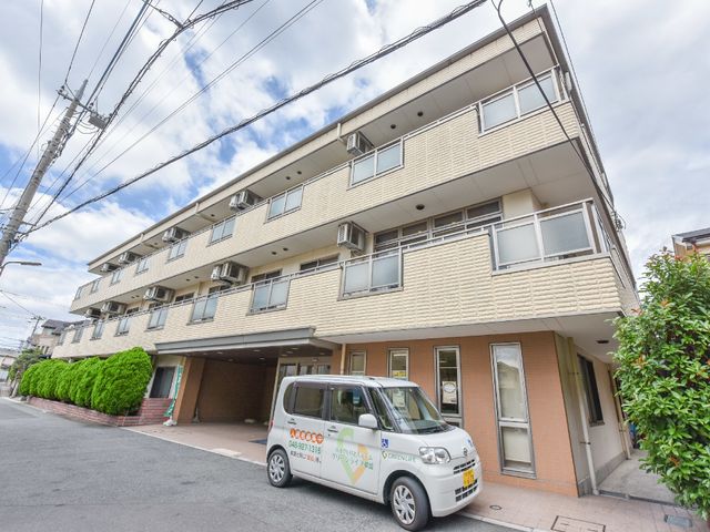 外観の建物と車 施設 明るい色合いの建物前には、緑豊かな植栽が配され、訪れる方をやさしく迎え入れます。駐車スペースもあり、便利な立地が魅力です。