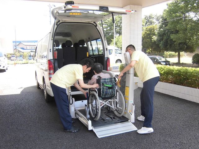 福祉車両での乗車場面 外観 車椅子利用者の安全な乗車をサポートするスタッフの様子です。快適な移動が可能です。