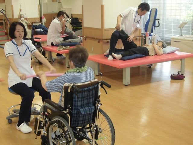 元気な運動風景の機能訓練室 機能訓練室 明るい空間で、利用者の方々がスタッフと一緒にリハビリを行っています。和やかな雰囲気です。
