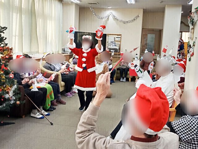 クリスマスイベント中のリビング リビング 広々としたリビングで、スタッフと利用者が一緒にクリスマスイベントを楽しんでいます。参加者同士の交流が活発で、和やかな雰囲気です。