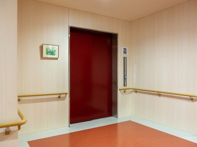 赤い扉のエレベーター エレベーター 手すりが設置された明るい通路にエレベーターがあります。利用者の移動がしやすい環境が整っています。