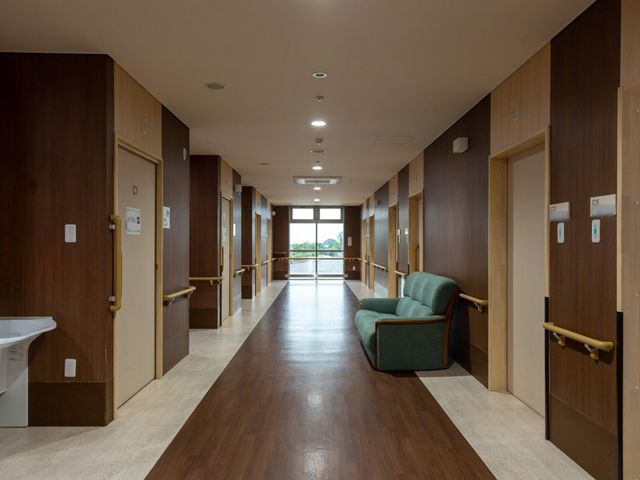清潔な廊下と木製ドア 通路 機能性と落ち着きを兼ね備えた廊下です。休憩できる座席も配置され、温かみのあるデザインを採用しています。