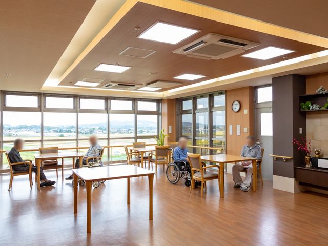 広々とした共有スペース 食堂 開放感あふれる休憩スペースで、入居者がゆったりとくつろいでいます。大きな窓からは明るい日差しが室内を照らし、温かな雰囲気を演出しています。