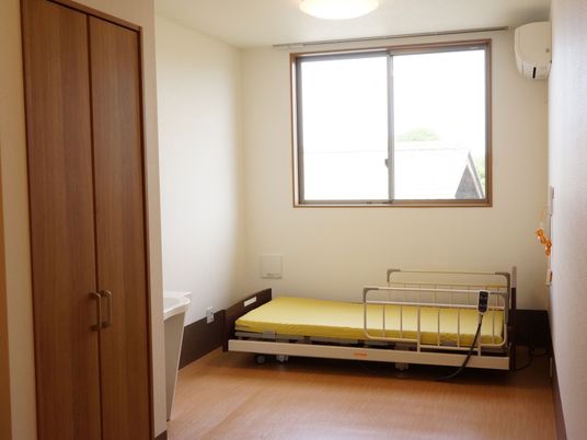 木目調の床と白い壁でつくられた居室である。介護用のベッドが完備され、両側にはベッドガードが備え付けられている。