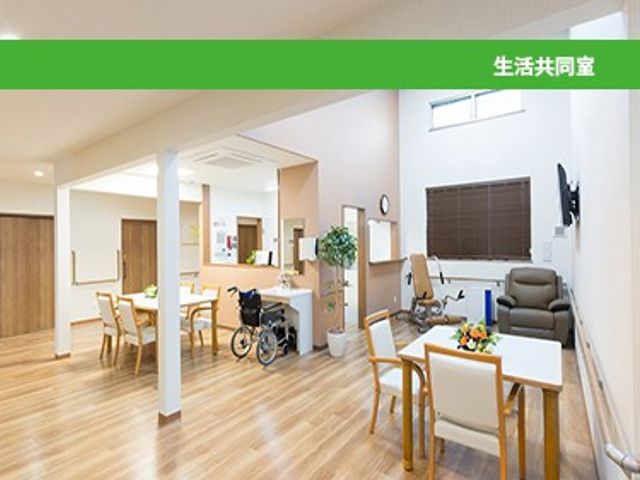 明るい生活共有室 リビング   自然光が入り、木目調の床が広がる明るい共用スペースです。車椅子でも動きやすそうなゆったりした配置で、くつろぎやすい雰囲気です。