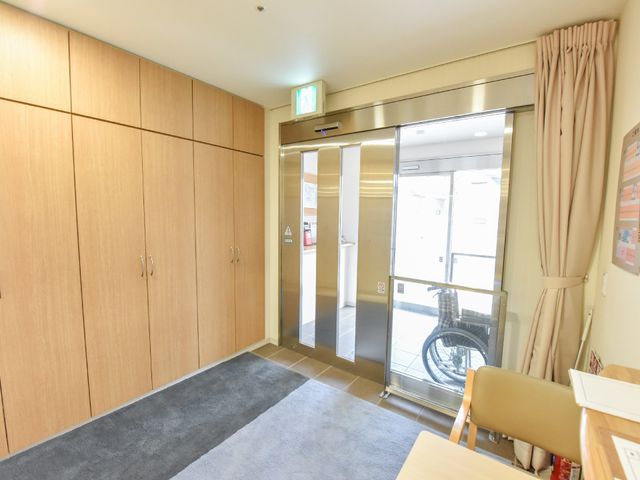 エレベーターとエントランス エントランスホール 温かみのある木目調のエントランスです。出入りがしやすい自動ドアが備わっており、明るく開放的な雰囲気を提供しています。
