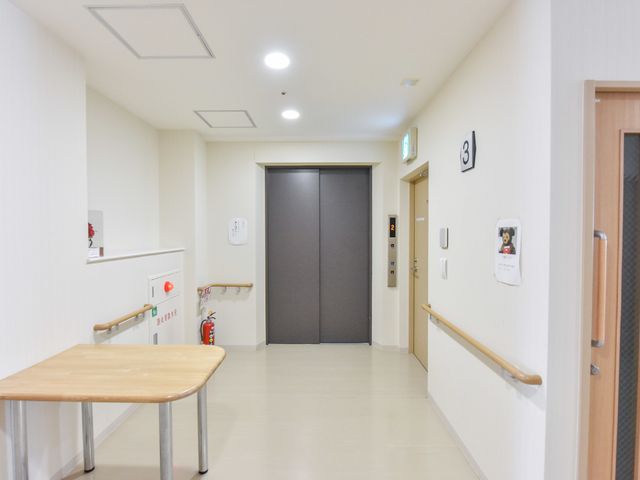 廊下の清潔なイメージ エレベーターホール 廊下は清潔で明るく、手すりが設置されており、安全に移動ができる環境が整っています。散歩や移動時の気分転換にもなります。
