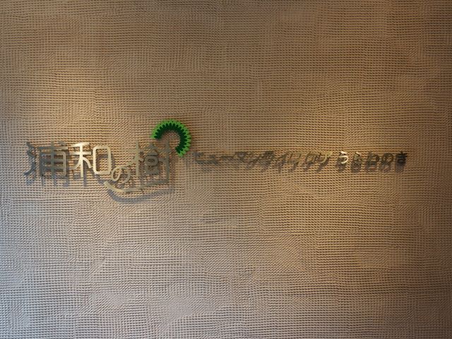 壁に掛かる施設の看板 温もりを感じるデザインの看板がお迎えします。こちらでの業務では、利用者様の心地よさを大切にする気配りが求められます。
