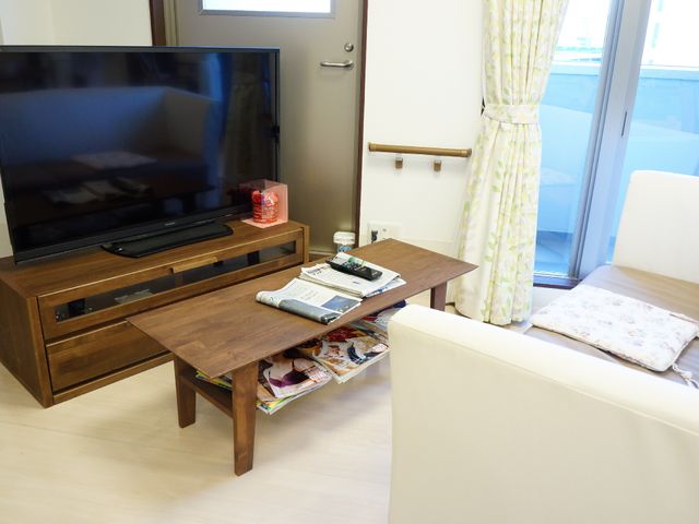 明るい居間の一角 快適な居住空間を提供しており、白いソファとテレビが配置されています。窓から自然光が差し込み、居心地の良さを感じさせる空間です。