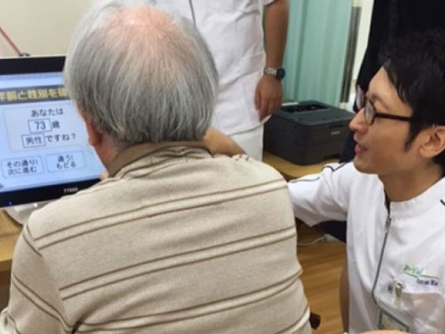 機能訓練の様子 診察 明るい表情を交わしながら、専門スタッフが入居者さまの運動サポートを行っています。日々の健康維持に努める姿が見受けられます。