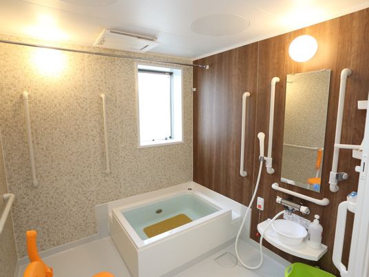 浴室の壁は、木目調とタイル張りとが共存しているデザインである。縦横にいくつもの手すりを設置して安全面に配慮している。