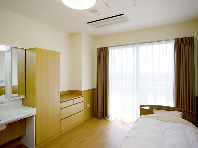 明るい個室の居室 居室 ゆとりのある個室で、木目調の家具が心地よい空間を演出しています。窓からは自然光が差し込み、明るく開放的な雰囲気です。