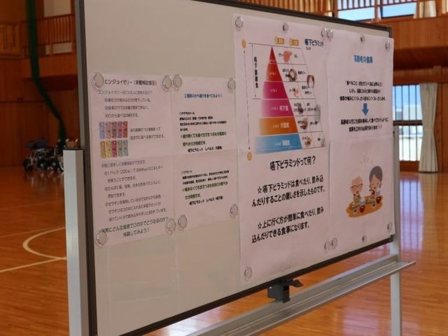掲示板のある多目的室 多目的室   木目調の広い空間に、案内を掲示したボードが置かれています。体操やレクリエーションにも使いやすそうな落ち着いた場です。