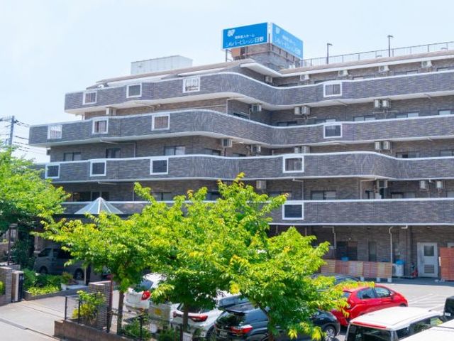 外観 外観 落ち着いた色合いの外壁が印象的な建物です。前面には木々があり、駐車スペースも見えます。
