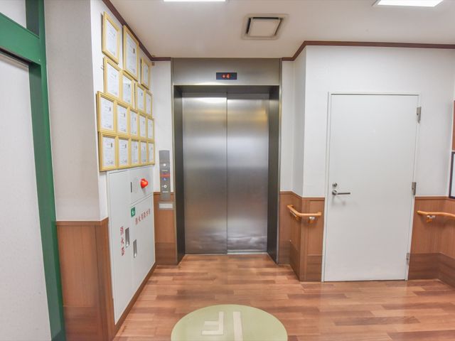 清潔な廊下とエレベーター エレベーター  スタッフや利用者様の行き来に便利なエレベーターが設置されており、すぐ横にはお知らせ等を掲示する掲示板も備えられています。