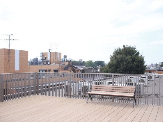 ３階建ての施設の屋上には、デッキが張りめぐらされており、フェンスの手前にベンチが置かれている。周辺の緑や建物が見渡せる。