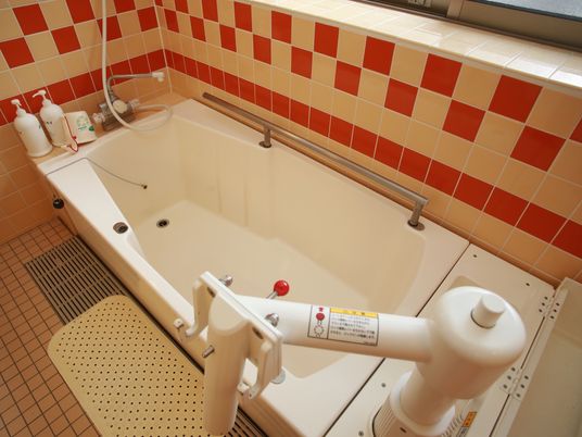 タイル張りの浴室の窓側に、四角い浴槽が設置されている。壁側にステンレス製の手すり、浴槽の手前に滑り止めマットがある。