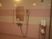 サムネイル タイル張りの浴室にシャワーと鏡が設置されている。シャワーの右側に金属製の網状の棚があり、ポンプ式のボトルや手桶が置かれている。