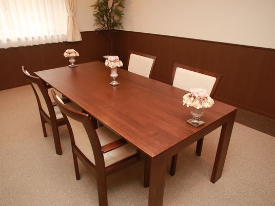 濃い茶色のテーブルに椅子が４脚据えられている。パステルカラーの花が挿してある光沢のある花瓶が３つ並べられている。