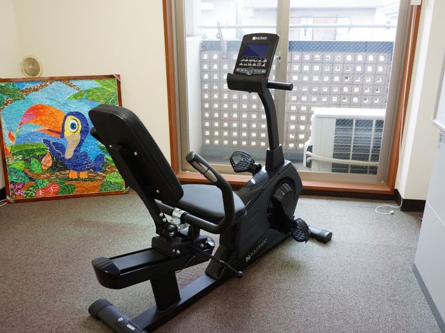 運動器具とアート作品 エアロバイク 窓際に置かれたエクササイズバイクは、健康維持に役立ちます。壁に掛けられた色鮮やかなアートが空間を明るく彩っています。