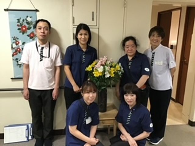 元気なスタッフと花の装飾 スタッフイメージ チームワークを大切にするスタッフたちと、充実した環境で介護の仕事に臨みましょう。あなたも私たちの一員に。