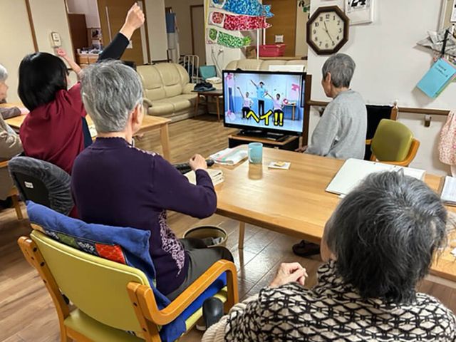 和やかな居室の様子 居室 笑顔で手を挙げている方々がいる、居心地の良さそうな空間です。寛ぎながらの交流が楽しめる場所となっています。