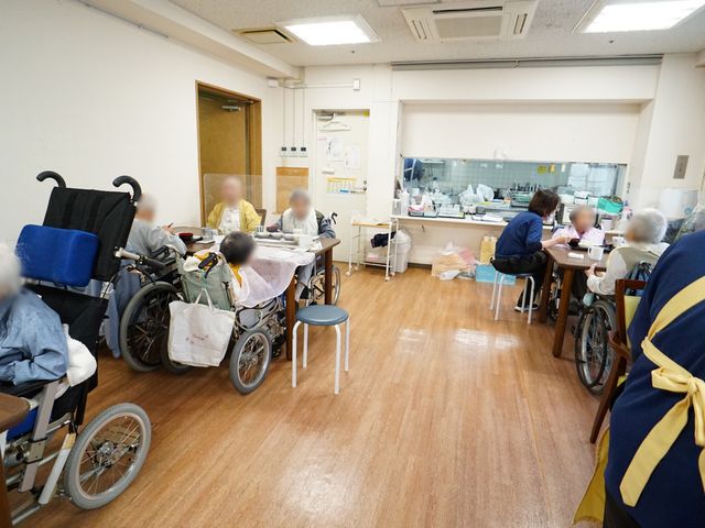 ゆったりとした居室 共有スペース 木目調で温もりのある居室で、ゆったりとした時間を過ごされています。スタッフは利用者様のそばで丁寧なサポートを行っております。