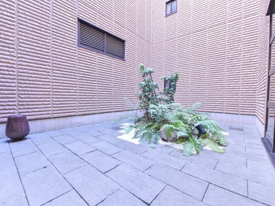施設の写真 タイルの敷かれた中庭は木々が植えられている。周りの壁にはテクスチャが施されデザインの整った空間に仕上がっている。